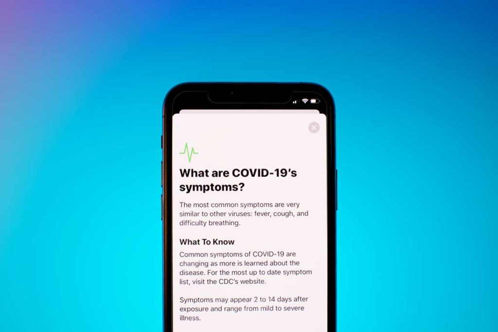 a cell phone with coronavirus website displaying symptoms against blue gradient background