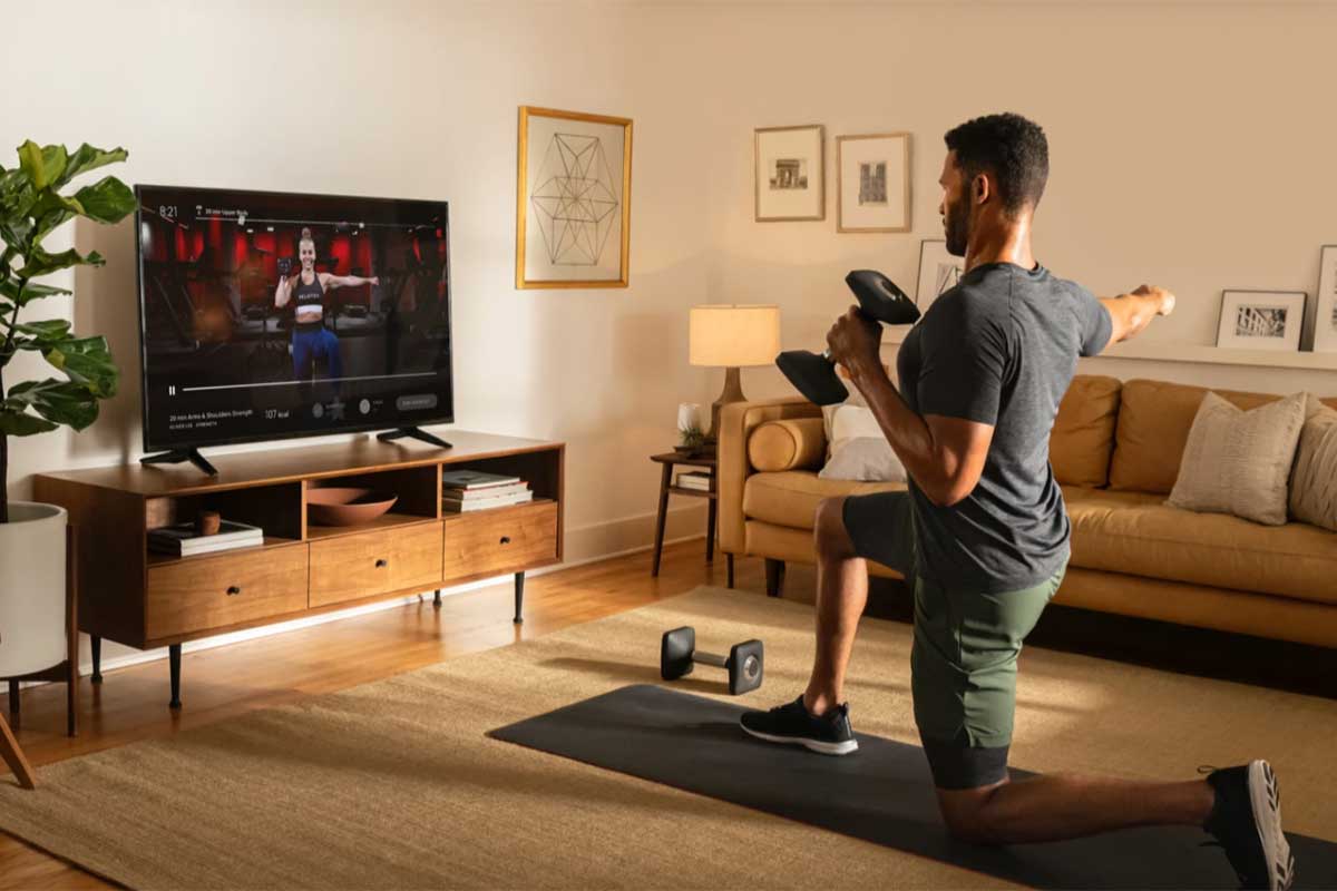 a man exercising in a living room while watching the peloton app on the big screen tv