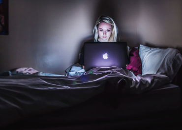 a woman watching tv on her laptop on her bed