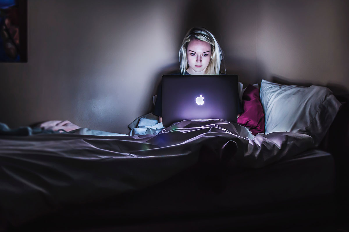 a woman watching tv on her laptop on her bed